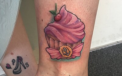 Ein rosa Cupcake Tattoo auf der unteren Wade einer Frau