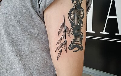 Kleines Black & Grey Tattoo in Form einer Pflanze auf dem Oberarm