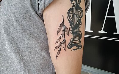 Small Black &amp; Grey Tattoo in the shape of a plant on the upper arm