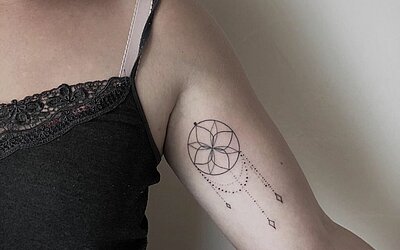Ein Traumfänger Tattoo auf dem linken Oberarm einer Frau