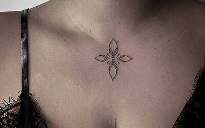 Ein kleines Tattoo als Ornament über dem Schlüsselbein zentriert bei einer Frau 
