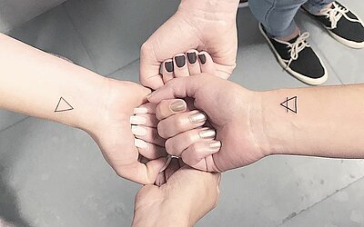 Vier Freunde zeigen ihre frischen Dreieck Tattoos am Handgelenk