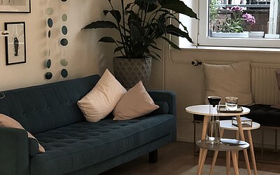 Eine grüne Couch mit einer großen Palme dahinter und einem Holz und Glastisch davor
