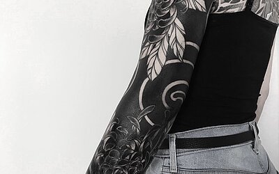 Ein Blackwork Tattoo mit vielen flächendeckenden schwarzen Stellen und schwarzen Blumen